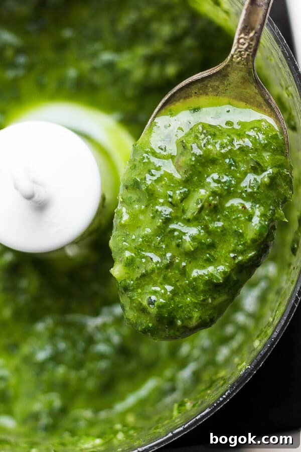 A spoon lifting out some basil vinaigrette out of a small food processor.
