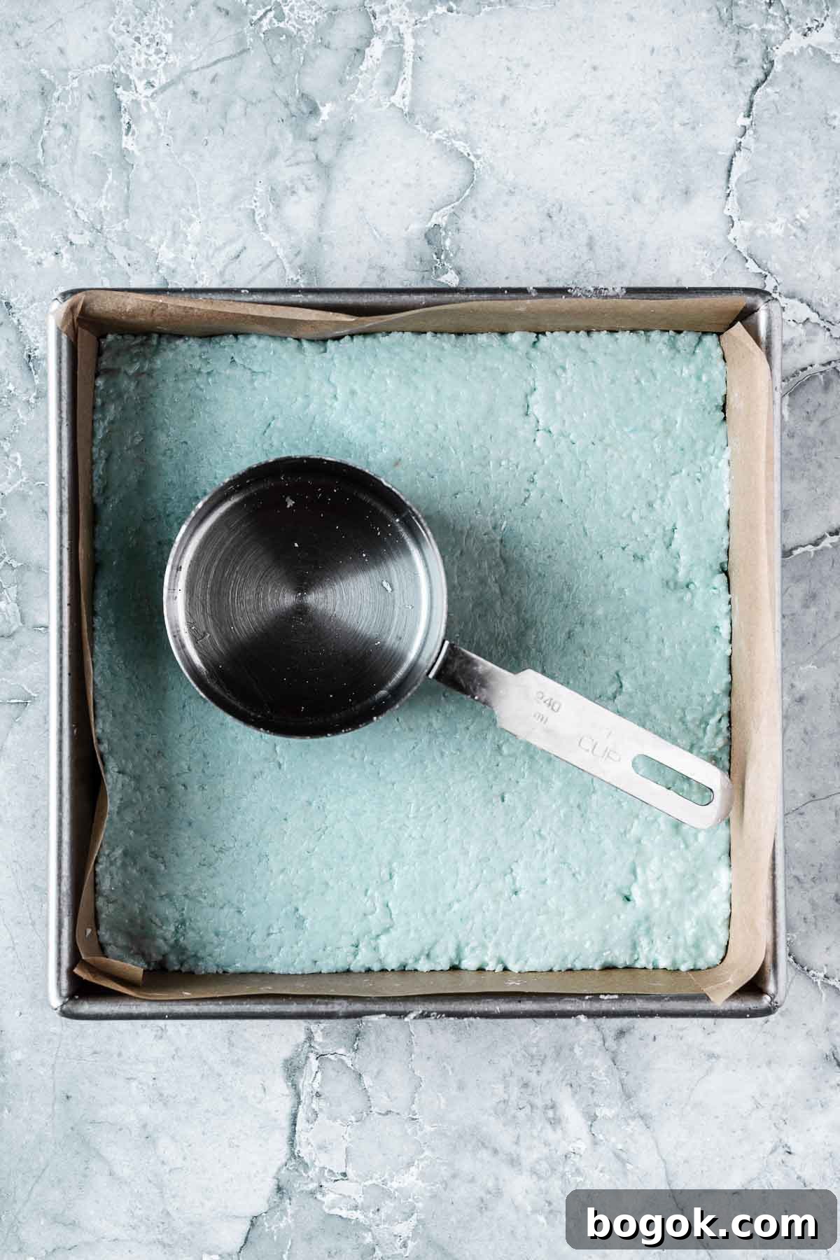 Classic Pink Coconut Ice Candy Recipe 10 The blue top layer of candy being compacted with a measuring cup.