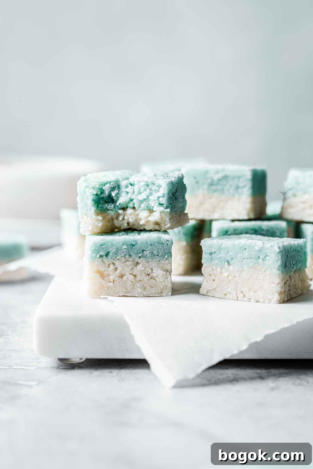 Classic Pink Coconut Ice Candy Recipe 5 Squares of blue and white coconut ice stacked up with a bite out of one.